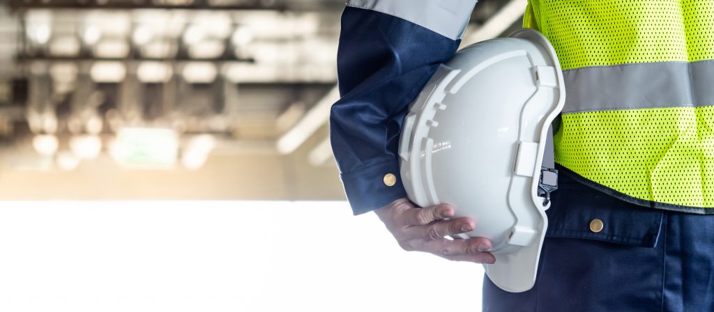 A close up photo of a maintenance technician's arm holding a white hard hat.