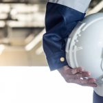 A close up photo of a maintenance technician's arm holding a white hard hat.